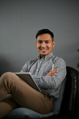 Fototapeta premium A smart Asian man or businessman sits with arms crossed on a black leather chair