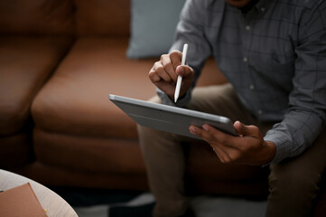 Close-up image of an Asian man using his digital tablet while sitting on a sofa