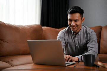 Handsome Asian businessman using laptop, working his business tasks in a living room.