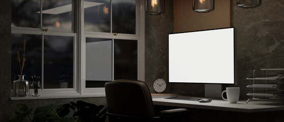 Modern home office at night with PC computer blank screen mockup on a table near the window.