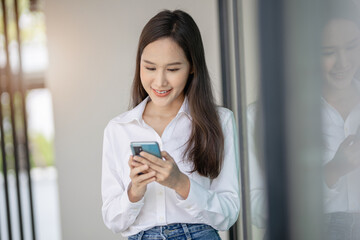 Millennial asian young woman looking mobile phone laughing with good news or discount voucher for...