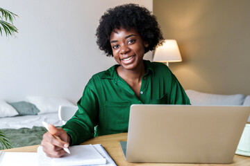Happy businesswoman with pen and laptop sitting at desk