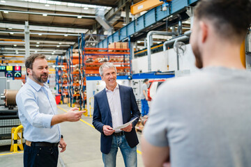 Smiling manager with businessman discussing with employee at factory