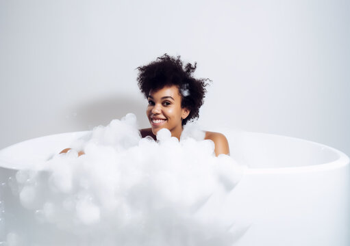 Woman in a bathtub with soap, foam and bubbles, looking happy and relaxed. African American ethnicity, Isolated on white background. Illustrative Generative AI. not a real person.