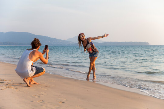 Man photographing girlfriend enjoying near shore at beach