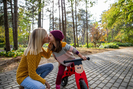 Daughter with bicycle kissing mother on footpath at park