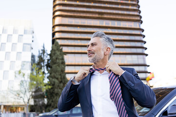 Mature businessman removing tie in front of building