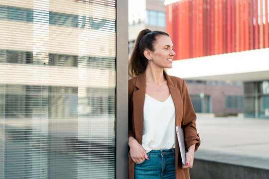 Smiling businesswoman with hand in pocket leaning on wall