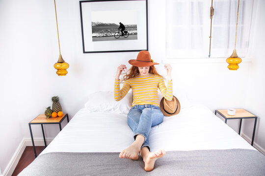 Woman wearing hat sitting on bed in hotel room