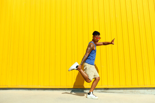 Man showing dance moves in front of yellow wall on sunny day