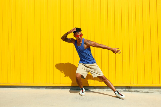 Young man dancing in front of yellow wall on sunny day
