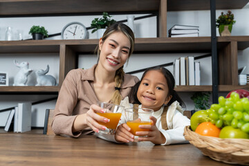 Beautiful mother drink orange juice into glass whit her lovely daughter