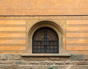 Figured metal lattice with a cross on a window on a stone wall