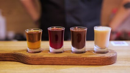 Bartender places a tasting flight of spirits in bar. Set includes different liquors with unique flavors and aromas. The set is beautifully arranged with shot glasses highlighting colors and textures.