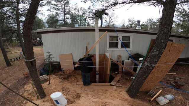 Time lapse and wide angle shot of two men pulling long pipe from hole while working on home made water well. One man stand on the mobile house roof.