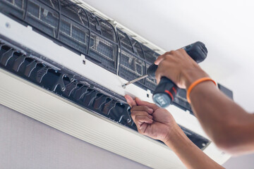Repairman using a screwdriver fixing modern air conditioner, Male technician cleaning air conditioner indoors, Maintenance and repairing concepts