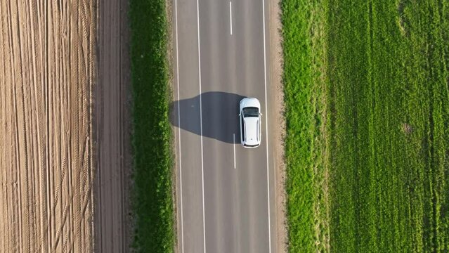 white minivan car slowly drives on a asphalt road among the fields at sunset