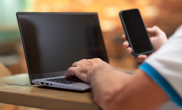 Defocused senior man sitting at bar table using laptop and mobile phone. Mature caucasian man typing on keyboard in business work - Powered by Adobe