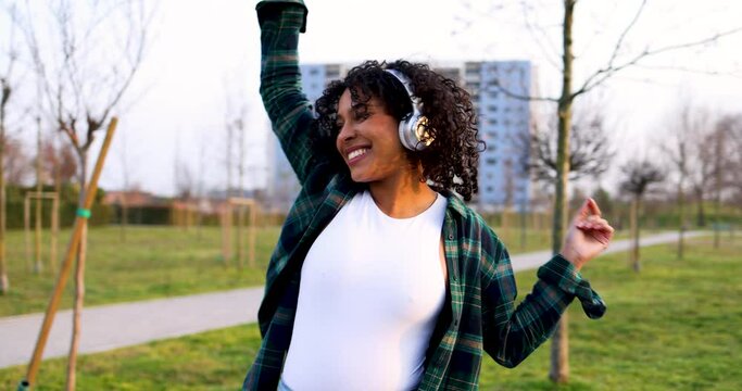 Dancing woman with headphones listening music in urban park