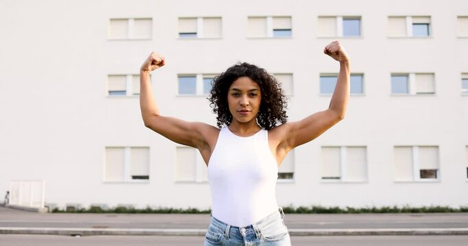 Young woman flexing muscles in front of buiilding
