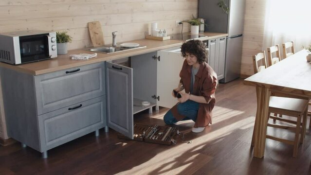 Caucasian woman failing to repair broken sink drain in kitchen and calling for professional plumber