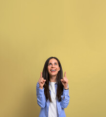 Portrait of cheerful young woman pointing upwards towards copy space against yellow background. Beautiful female with long hair smiling and looking up at blank space