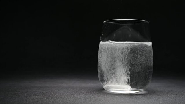 Effervescent tablet in transparent glass cup on dark background, close-up, space for text.