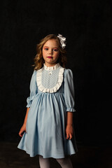 Sad little cover girl in image of doll in blue dress at black background, pensive looking at camera. Studio shot of cute child isolated with light and shadow. Kids emotion concept. Copy ad text space