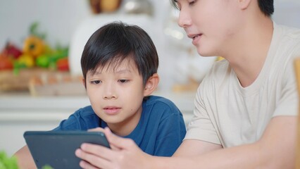Asian father teaching little son using digital tablet for learning online at home in social distancing during self quarantine. Online education concept