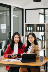 Two Asian businesswoman discuss investment project working and planning strategy with tablet laptop computer in office.