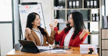 Two Asian businesswoman discuss investment project working and planning strategy with tablet laptop computer in office.