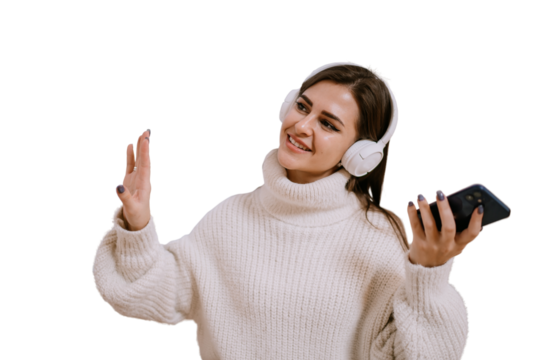 Beautiful brunette female model in white sweater and headphones dancing home against transparent background, smiles enjoying music on weekend. Domestic leisure, relaxation.