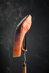 Smocked salmon piece with natural smoke on a black background.