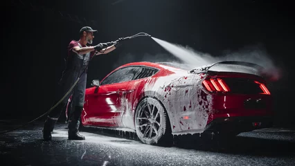 Fototapeten Automotive Detailer Washing Away Smart Soap and Foam with a Water High Pressure Washer. Red Performance Car Getting Care and Treatment at a Professional Vehicle Detailing Shop © Gorodenkoff