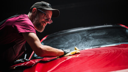 Car Wash Expert Using a Microfiber Cloth to Dry Up a Red Modern Sportscar. Adult Man Cleaning Away...