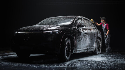 Professional Car Wash Specialist Spreading Foam with a Soft Sponge to Prepare a Modern Black Electric SUV with Contemporary Design at a Dealership Car Center. Commercial Studio Photo for Advertising