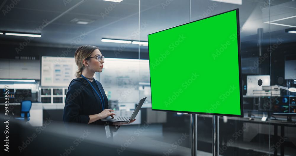 Poster Beautiful Lead Software Engineer Standing Alone in a Meeting Room, Using Laptop and Looking at a TV with Green Screen Mock Up Display with Potential Information Created by Development Department
