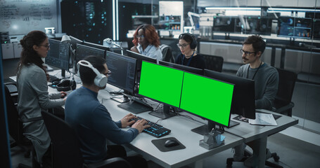 Group of Diverse Multicultural Men and Women Working on Desktop Computers in a Research Center. Young Software Developer Working on a Computer with Two Green Screen Mock Up Displays