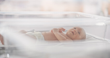 Adorable Small Caucasian Newborn Child Lying in Hospital Bed in a Nursery Clinic. Little Playful and Healthy Baby. Medical Health Care, Maternity and Parenthood Concept - obrazy, fototapety, plakaty