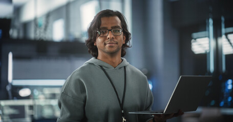 Young Indian Software Engineer Using Laptop Computer in Data Center, Looking at Camera. Successful...