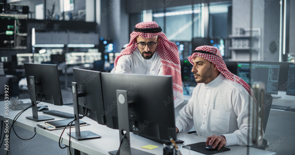 Aufkleber Young Team of Arab Specialists Working on Computers and Having a Conversation at a Workplace. Two Male Software Developers Discussing a Solution for Their Generative Artificial Intelligence Project