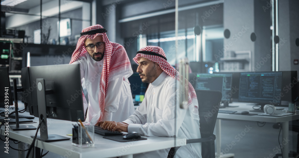 Poster Two Young Saudi Software Engineers Use Desktop Computer to Discuss a Technological Project in a Modern Industrial Office. Arab Scientists Work in Research and Development Center