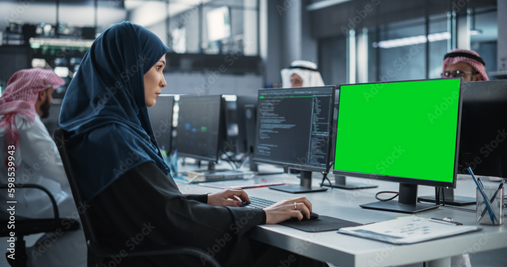 Poster Arab Female Software Developer Working on Desktop Computer with Green Screen Mock Up Display. Young Middle Eastern Specialist Testing Programming Code for an Innovative Big Data Blockchain Project