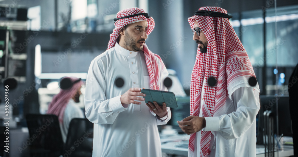 Poster Two Multiethnic Arab Colleagues Having a Conversation While Busy Working on a Software Development Project. Engineer Talking with a Middle Eastern Project Manager, Using Tablet Computer in Office
