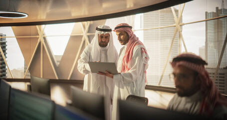 Two Young Muslim Financial Advisers Use Laptop Computer to Discuss a Stock Market Strategy in a Modern Industrial Office. Arab Managers Work in a Banking Research and Development Center