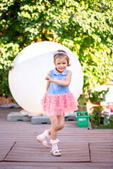 A cheerful little girl plays in the park on the lawn in a beautiful dress rejoices in the summer. Beautiful white girl smiling while walking in the courtyard of the house.