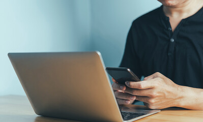Fototapeta premium businessman's hands using a phone at his desk in the rear, and a young male sitting at a wooden desk typing on a phone