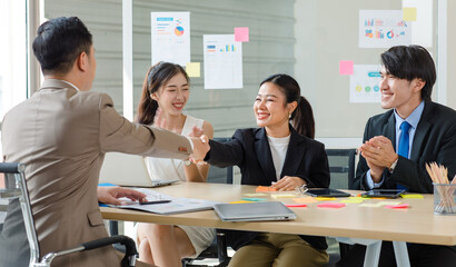 Asian professional successful businesswoman sitting smiling shaking hands greeting with unrecognizable businessman in formal business suit while male female colleagues clapping hands celebrating