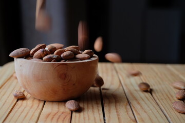 Peeled almonds in a wooden bowl and some scattered nuts on black background	
