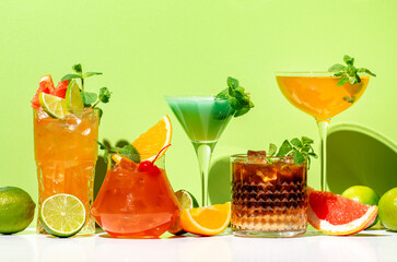 Alcoholic drinks with mint, summer cocktail party. Multi-colored low-alcohol beverage glasses set. Green background, hard light, shadow pattern